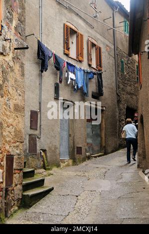 Bergdorf Roccatederighi, Toskana, Italien, antike Straßenszene, Waschen hängt an den Fenstern in einem engen Durchgang, ein Fußgänger, Stockfoto