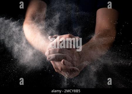 Mehlexplosion in männlichen Händen auf dunklem Hintergrund. Teigzubereitung, Kochkonzept. Stockfoto