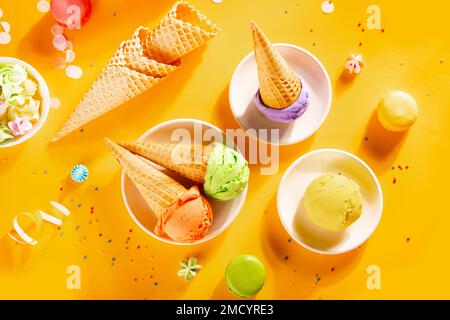 Verschiedene bunte Eislöffel oder -Bälle mit Waffelmuscheln auf gelbem Hintergrund. Draufsicht Stockfoto