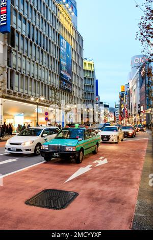 Tokio, Shibuya. Abend blaue Stunde Blick entlang Jingu-Mae dori Shopping Street. Zwei Fahrstreifen des Gegenverkehrs, hauptsächlich Taxis. Negativer Platz. Stockfoto