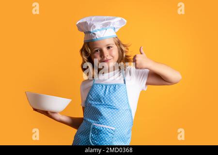 Lustiger Kinderkoch mit Küchenteller, Studioporträt. Der Kinderkoch bereitet Speisen auf isoliertem Studiohintergrund zu. Kinder kochen. Mit Teenager-Junge Stockfoto