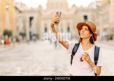 Porträt fröhliche junge Frau, die Selfie-Fotos macht und in die Kamera schaut, während sie im Stadtzentrum auf dem Platz ist. Bloggerin Reisende Stockfoto