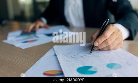 Finanzanalyst prüft Daten, Diagramme und Diagramme, schreibt auf Papier, sitzt am Schreibtisch im Büro, schließt Stockfoto