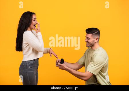 Ein glücklicher Millennials-araber, der kniet, einen Ring mit Schmuck in der Hand hält, der überraschten Dame einen Heiratsantrag macht Stockfoto