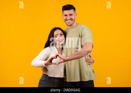 Lächelnder arabischer Typ und Frau, die sich umarmen, das Herz mit aneinander liegenden Händen signieren lassen Stockfoto