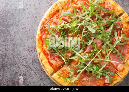 Pizza Prosciutto gekocht mit Tomatensoße, Mozzarella, Schinken, Rucola, Parmesan Nahaufnahme auf einem Holzbrett auf dem Tisch. Horizontale Draufsicht von oben Stockfoto