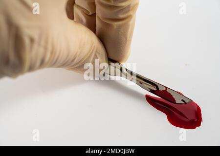 Blut gefärbt steriler Edelstahl Präzisionsmesser Gesundheit professionelle Chirurgen Skalpell isoliert auf weißem Hintergrund mit Blutpool Stockfoto