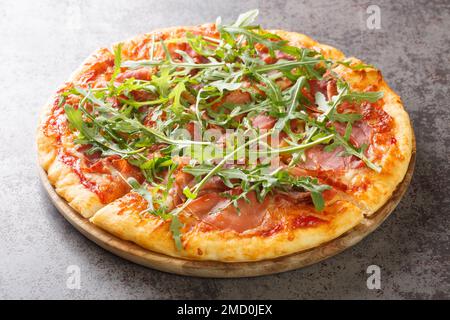 Heiße Pizza mit Prosciutto und Rucola Nahaufnahme auf einem Holzbrett auf dem Tisch. Horizontal Stockfoto