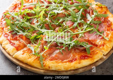 Pizza Prosciutto gekocht mit Tomatensoße, Mozzarella, Schinken, Rucola, Parmesan Nahaufnahme auf einem Holzbrett auf dem Tisch. Horizontal Stockfoto