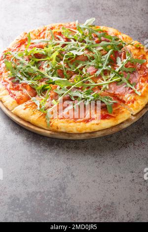 Prosciutto Pizza mit Käse, Tomatensoße und frischer Rucola Nahaufnahme auf einem Holzbrett auf dem Tisch. Vertikal Stockfoto