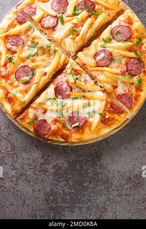 Americana Pizza mit pommes Frites, Würstchen, Käse und Tomatensoße aus der Nähe auf einem Holzbrett auf dem Tisch. Vertikale Draufsicht von oben Stockfoto