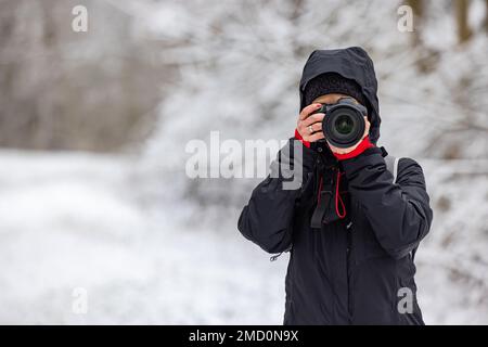 Weibliche Fotografin mit professioneller Kamera, die im Winter im Freien fotografiert Stockfoto