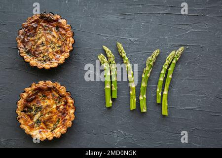 Vegetarischer Spargelquiche oder Torte auf schwarzem Hintergrund, gesunder Sommersnack, Draufsicht. Stockfoto