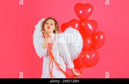 Valentinstag Amor. Weiblicher Engel in weißen Flügeln mit roten herzförmigen Ballons, die einen Luftkuss senden. Stockfoto