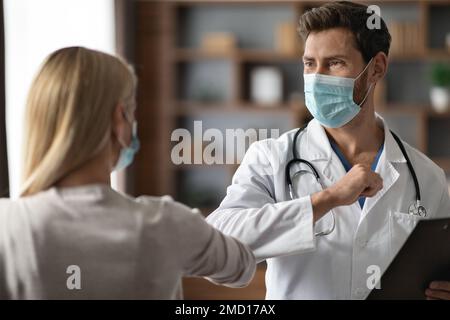 Männlicher Arzt In Medical Mask Ellenbogenstoßen Begrüßung Mit Weiblicher Patientin Stockfoto