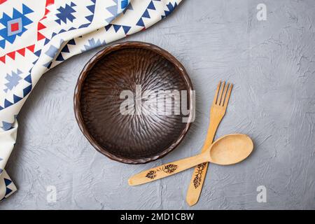 Alte Holzschüssel mit Holzbesteck und ethnisch gemustertem Stoff auf grauem Zementhintergrund Stockfoto