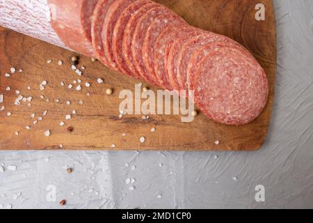 Dünne Salami auf einem Holzbrett, auf einem Zementtisch Stockfoto