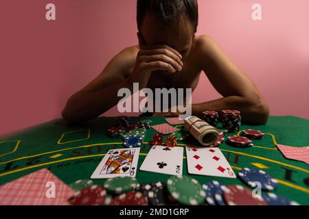 Unglücklicher junger Mann, der sich traurig, verzweifelt und gestresst fühlt, nachdem er sein Geld beim Poker und Blackjack in einem nächtlichen Casino verloren hat Stockfoto