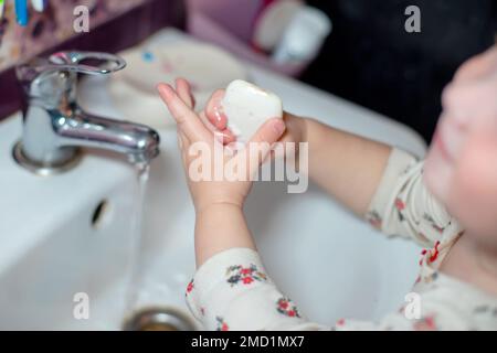 Ein kleines Mädchen wäscht sich im Bad die Hände mit weißer Seife. Ein Kind in der Nähe des weißen Waschbeckens wäscht sich die Hände Stockfoto