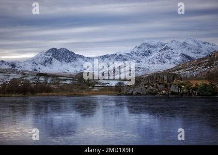 Mount Snowdon ist hier auf der anderen Seite des gefrorenen Sees von Llynnau Mymbyr im Tal von Dyffryn Mymbyr im Snowdonia-Nationalpark, Nordwales zu sehen. Stockfoto