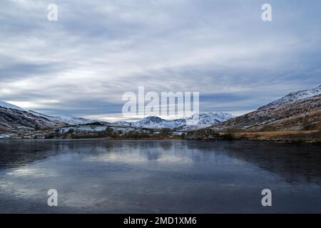 Mount Snowdon ist hier auf der anderen Seite des gefrorenen Sees von Llynnau Mymbyr im Tal von Dyffryn Mymbyr im Snowdonia-Nationalpark, Nordwales zu sehen. Stockfoto