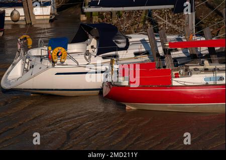 Ebbe am Strand Quay: Jachten mit rot-weißen Hüllen, die in glühendem braunem Schlamm am Flussbett des Flusses Tillingham, einem Nebenfluss des Flusses Rother in Rye, East Sussex, England, vertäut sind. Die Stadt war einer der mittelalterlichen Cinque-Häfen, aber heftige Stürme in den späten 1200s Jahren veränderten den Kurs des Rother, und Jahrhunderte der Silbung und Landrückgewinnung haben es 3,2 km vom Meer entfernt gelassen. Stockfoto