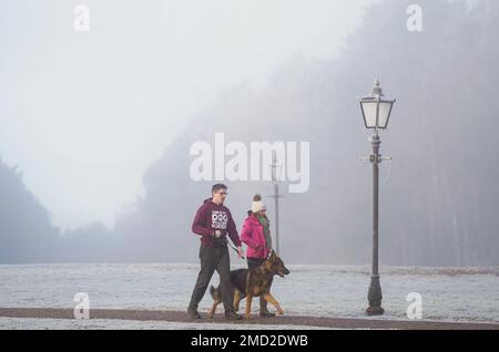 Die Leute gehen mit ihrem Hund durch das Sandringham Estate in Norfolk. Es wurde eine Reihe von Wetterwarnungen ausgegeben, die zu überfrierendem Nebel führen könnten, der zu Luftverschmutzung und schwierigen Fahrbedingungen führen könnte, wenn die Kälte beißt. Foto: Sonntag, 22. Januar 2023. Stockfoto