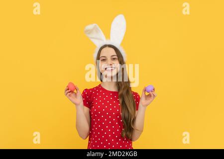 Porträt eines Teenagers mit Hasenohren, das ostereier auf gelbem Hintergrund isoliert hält. Stockfoto