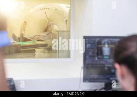 Im medizinischen Labor Patient durchläuft MRI oder CT-Scan-Prozess unter Aufsicht des Arztes und Radiologen im Kontrollraum, sie watche Verfahren und Stockfoto