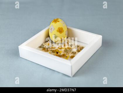 Gelbes Osterei aus Holz mit gepressten getrockneten Blumen. Modische Frühlingsfarben. Kunstideen für Ostern. Stockfoto