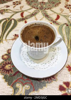 Authentischer orientalischer türkischer Kaffee auf traditionellem Zierhintergrund. Schwarzer Kaffee in einer kleinen weißen Tasse. Stockfoto