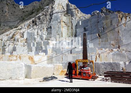 Eine Frau, die eine Motorsäge schneidet und Marmorblöcke im Carrara-Marmorbruch, Carrara, Italien, ansieht Stockfoto