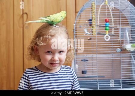 Ein kleines Mädchen mit einem Boogie auf dem Kopf neben einem großen Käfig im Wohnzimmer. Stockfoto