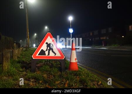 Ein dreieckiges Straßenschild und ein Verkehrskegel am Straßenrand bei Nacht für abgenutzte Autofahrer, die von Bauarbeiten vor ihnen betroffen sind, Stockfoto