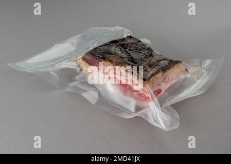 Guanciale Schweinebacken in vakuumverpackter Verpackung, versiegelt für Sous-Vide-Kochen auf grauem Hintergrund Stockfoto