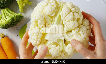 Frauenhände halten Blumenkohl. Nahaufnahme von oben, Rezept, Kochen, Konzept des Zubereitungsprozesses Stockfoto