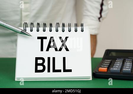 Geschäftskonzept. Auf einer grünen Oberfläche ist ein Taschenrechner, ein Mann zeigt mit einem Stift auf ein Notizbuch mit der Aufschrift "Steuerrechnung" Stockfoto