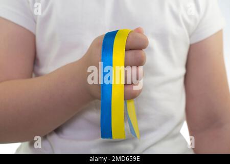Ein Mädchen in einem weißen T-Shirt hält ein gelb-blaues Band in der Hand (Nahaufnahme). Staatsflagge der Ukraine. Nationales Symbol der Ukraine. Patriot Stockfoto