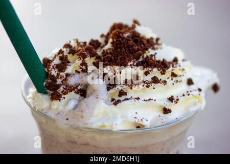 Frappe mit Kekskrümel, Schlagsahne, Schokoladenkrümel in Plastikglas mit grünem Papierrohr. Eiskaltes Getränk als Erfrischung für heißen Sommertag. Makrofoto Stockfoto