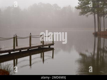 Morgennebel entlang des ruhigen Teiches und der hölzernen Anlegestelle Stockfoto