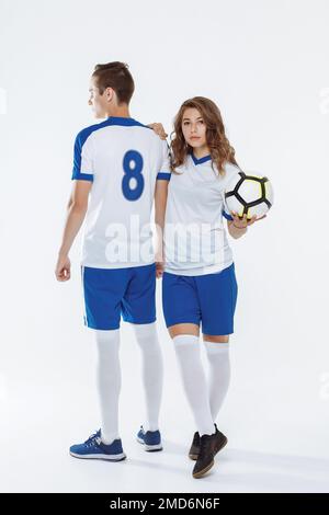 Mädchen und Mann in Fußballuniformen halten einen Fußball auf weißem Hintergrund Stockfoto