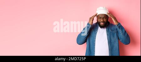 Bekümmerte schwarze Mann mit Kopfschmerzen, berühren Kopf und Grimacing mit betroffenen Gesicht, stehen über rosa Hintergrund Stockfoto