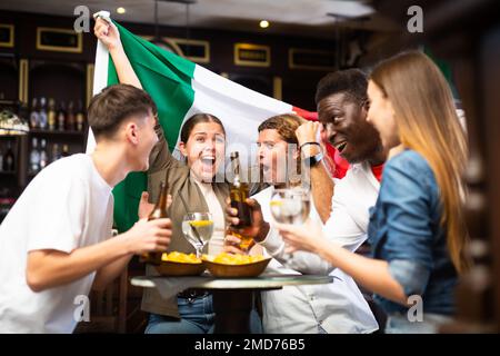 Emotionale, vielfältige Sportfans mit der Flagge Italiens mit Bier und Chips im Pub Stockfoto