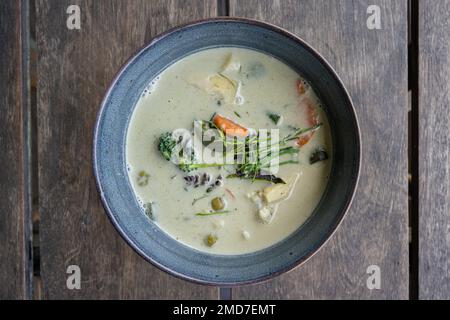 Blick von oben auf eine Schüssel mit grünem Thai-Gemüse-Curry auf einem Holztisch Stockfoto