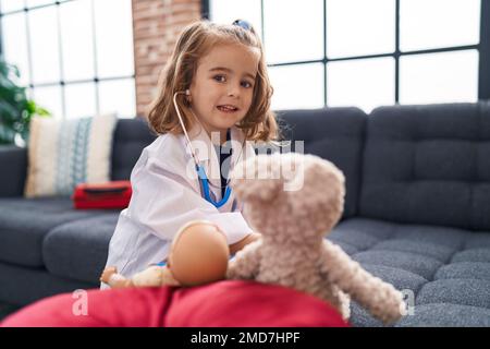 Ein bezauberndes, lateinamerikanisches Mädchen in Arztuniform, das zu Hause ein Baby auskultiert Stockfoto