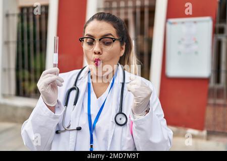 Junge hispanische Ärztin Frau, die Coronavirus-Infektion Nasentest macht Fischgesicht mit Mund und schielenden Augen, verrückt und komisch. Stockfoto