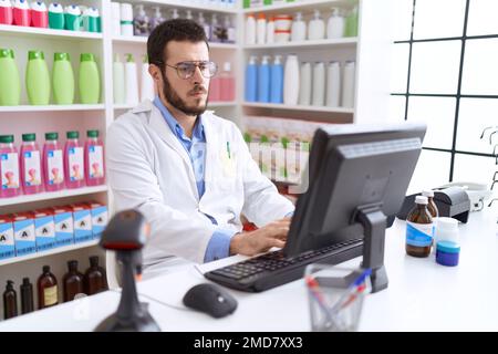 Junger hispanischer Apotheker mit Computer und Zweifelsausdruck in der Apotheke Stockfoto
