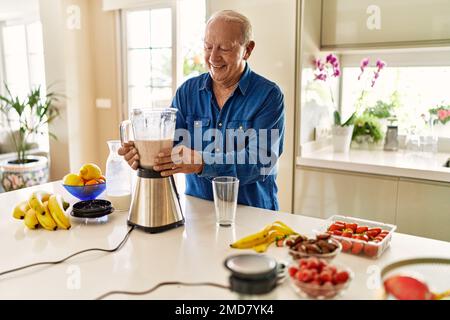 Ein Mann lächelt selbstbewusst und hält ein Glas Smoothie in der Küche Stockfoto