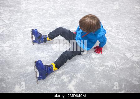 Ein Junge, der einen Sturz auf die Eisbahn erlitten hat. Temporäre Eislaufen-Installation Stockfoto