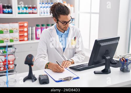 Junger hispanischer Apotheker, der auf einem Dokument in der Apotheke schreibt Stockfoto